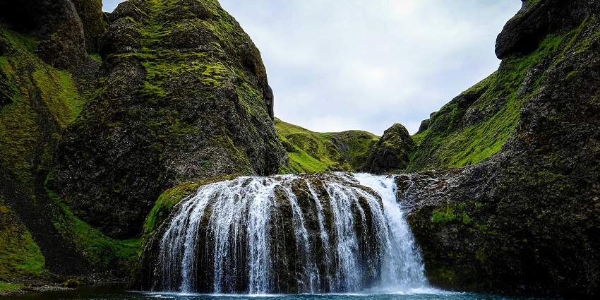 A captivating view of a waterfall surrounded by rocky mountains and cloudy skies.