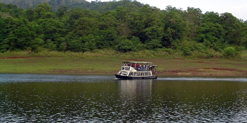Boat safari on tranquil lake in Ulipooni Wildlife Sanctuary, framed by lush forested hills.