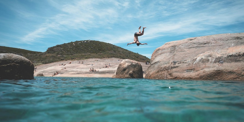 Man mid-air while cliff jumping into the ocean on a sunny day—things to do in gandikota