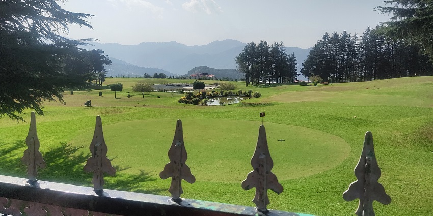 Scenic view of Naldehra Golf Course, surrounded by lush greenery and mountains.