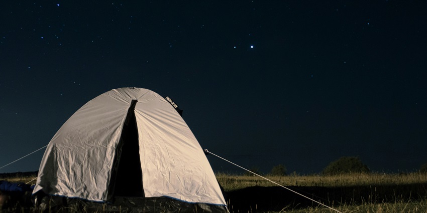 Grey tent view at night, surrounded by dark silhouettes of nature and a starry sky.