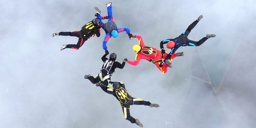 Group of skydivers in formation, descending through the sky with coordinated movements.