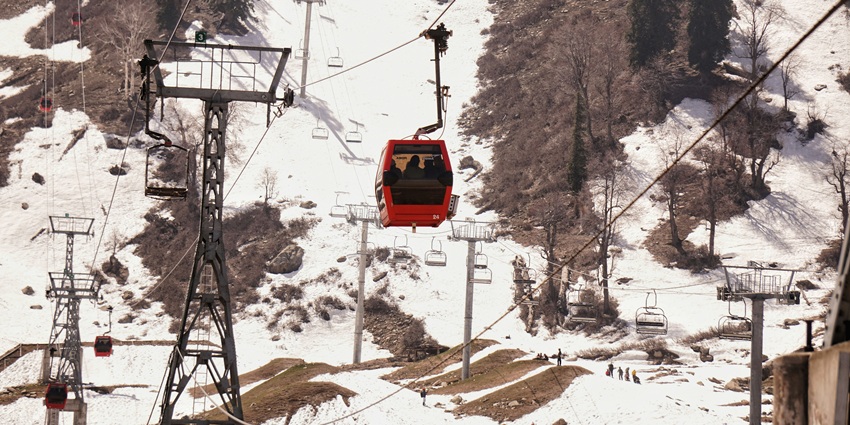 Ski lift ascends a snow-covered mountain in Gulmarg, Kashmir, showcasing beauty of the region.