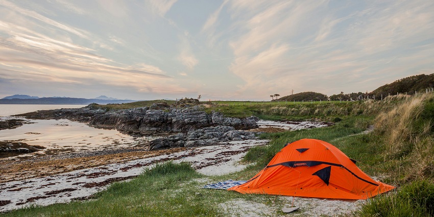 A mesmerising view of an orange tent near a body of water and greenery during the daytime.