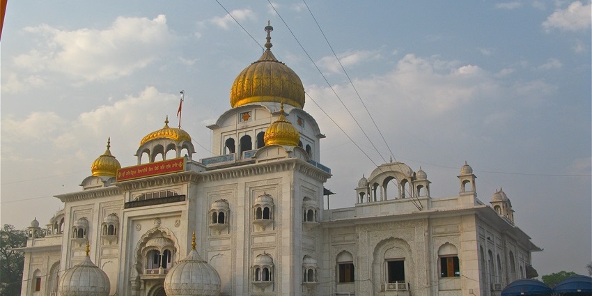 Front view of Gurudwara Bangla Sahib with domes, reflection pool, and devotees.
