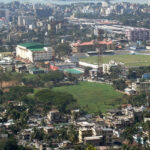 An aerial picture of a city with greenery, a cricket stadium, and housing apartments as seen during daytime