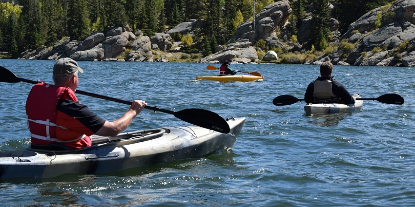 Three men riding kayaks on a serene body of water, enjoying a peaceful paddling experience