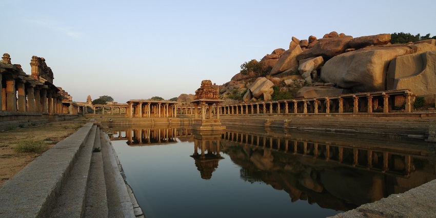 Ancient ruins of Hampi with intricate carvings and lush greenery surrounding them.