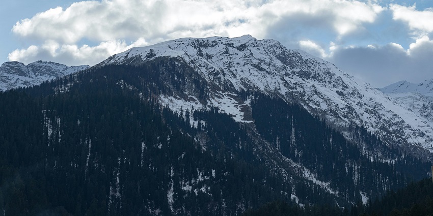 A stunning view of a snow-covered mountain range under dense clouds during the day.