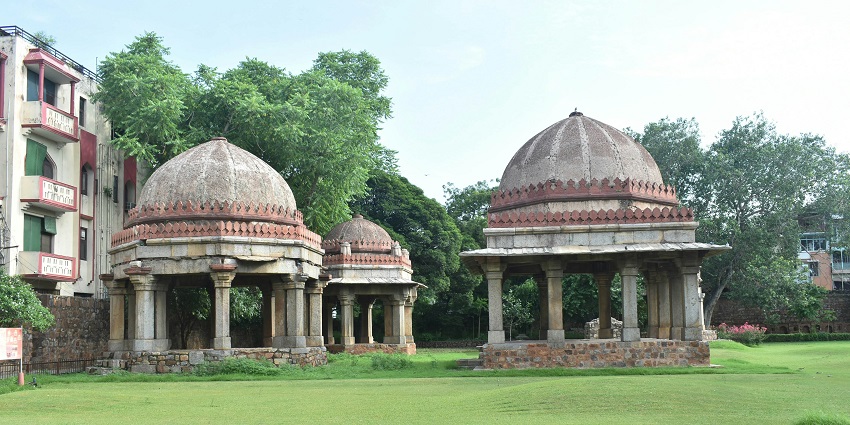A breathtaking view of Hauz Khas Village with red and white tombs around greenery.