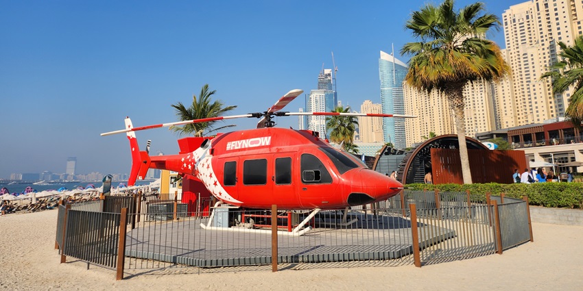 An orange-coloured helicopter parked at a helipad in Dubai, with palm trees and buildings in the background
