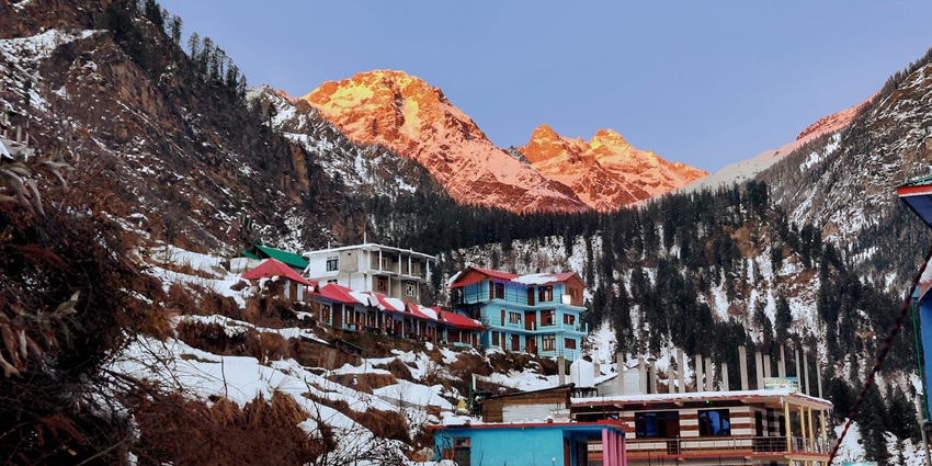 A scenic view of a small mountain village surrounded by the snowy peaks of Himalaya