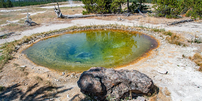 A serene hot water spring surrounded by lush greenery hills, steam rising gently.