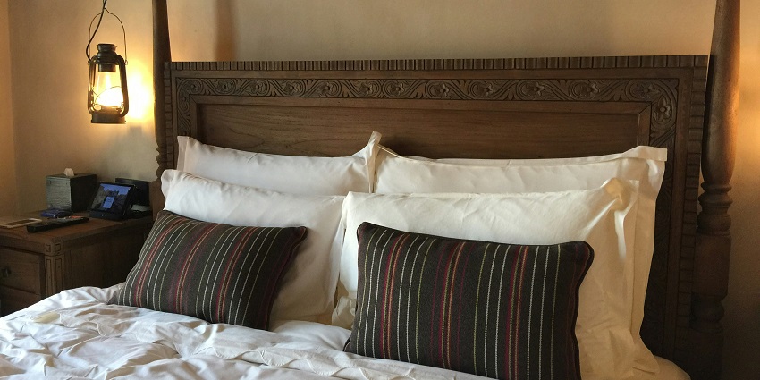 A picture of a hotel room with a wooden bed with white sheets and a hanging lantern.
