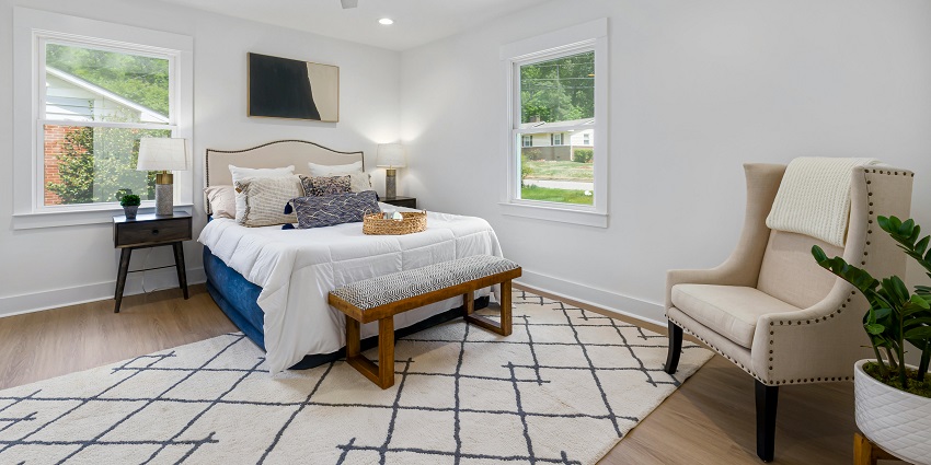Cosy white and brown bed by a large glass window, inviting natural light into the room.