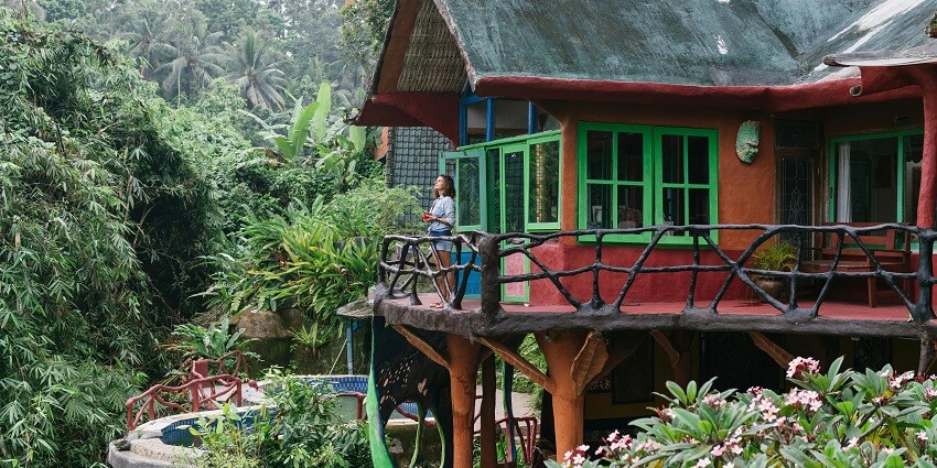 Picture of a woman standing on the balcony opf a hotel surrounded by the lush forest