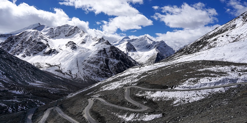 View of road constructed on snow-covered mountains and cloudy skies in the backdrop.