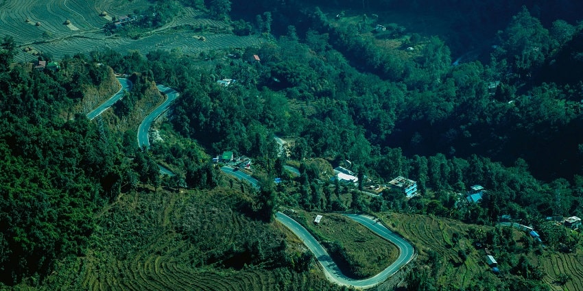 A view of a winding road in Gangtok surrounded by lush green meadows and houses.