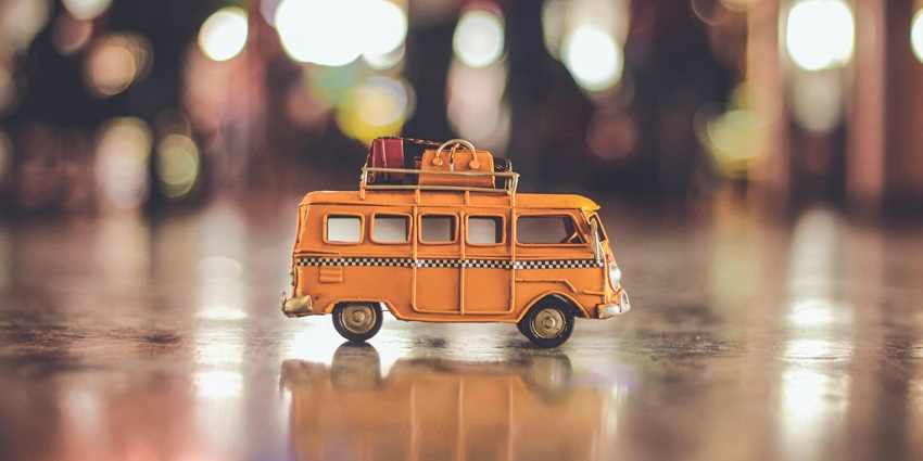 A selectively focused view of a yellow miniature bus with people in the background.