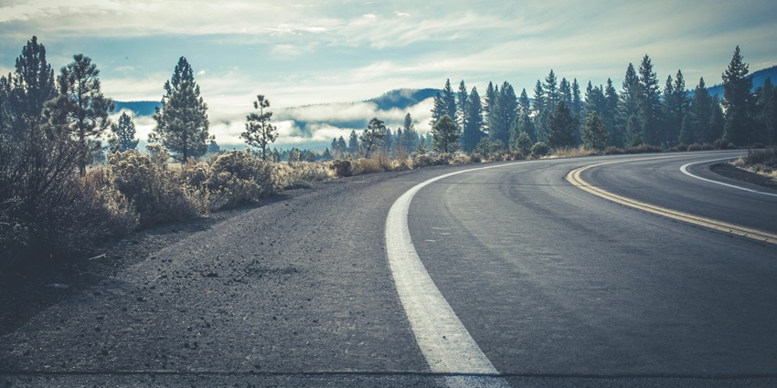 A stunning view of a winding road leading upto a mountain range during the daytime.