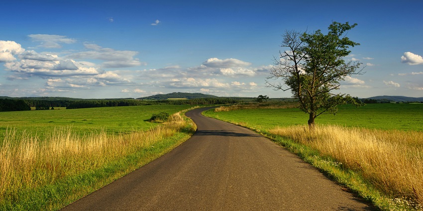 A stunning view of a narrow strip of road passing through a lush green grassland.