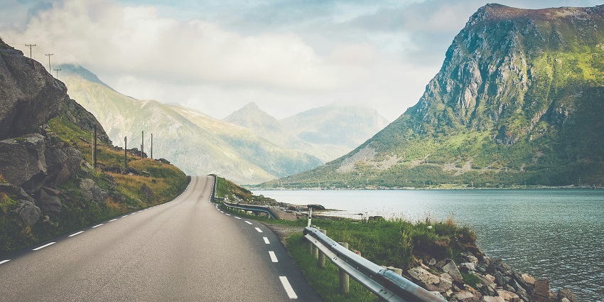 A stunning view of a narrow strip of road passing by a sparkling body of azure waters.