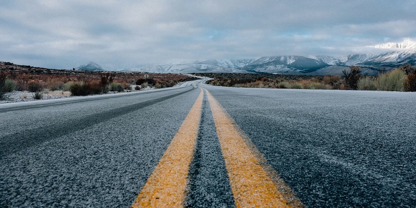 A stunning view of a road leading up to snow-covered mountains surrounded by greenery.