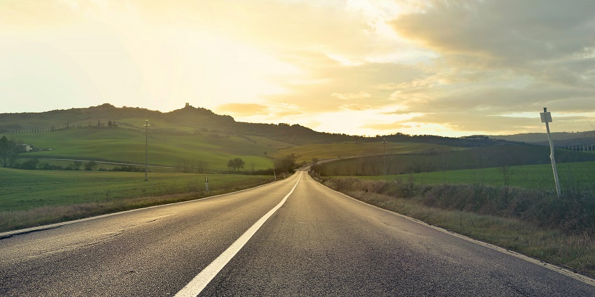 A fascinating view of a narrow strip of road leading up to a green valley during the day.