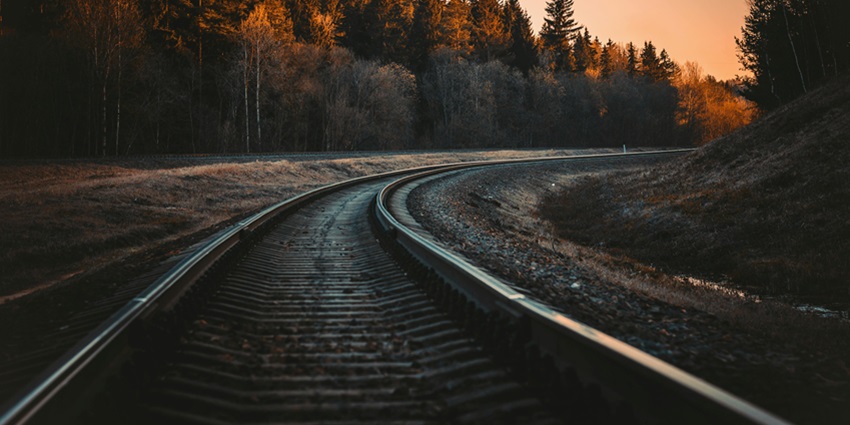 A view of a railway track surrounded by lush green trees during the evening time.