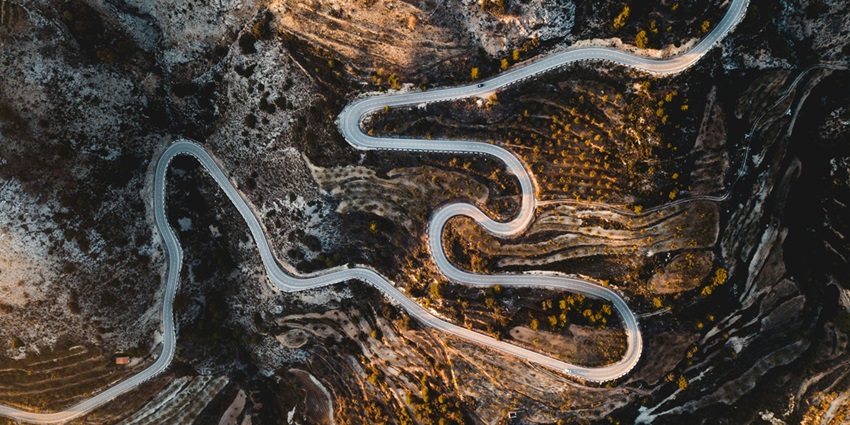 A mesmerising aerial view of a winding road encircled by lush green trees during the day.