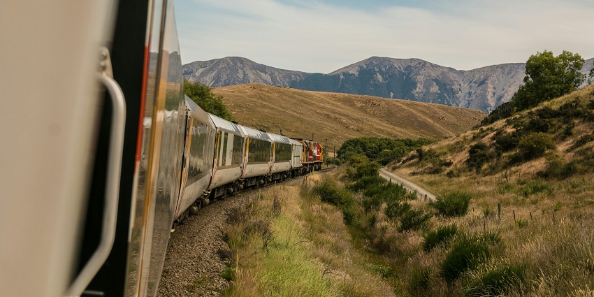 A stunning view of a lush green valley from a train with mountains in the background.