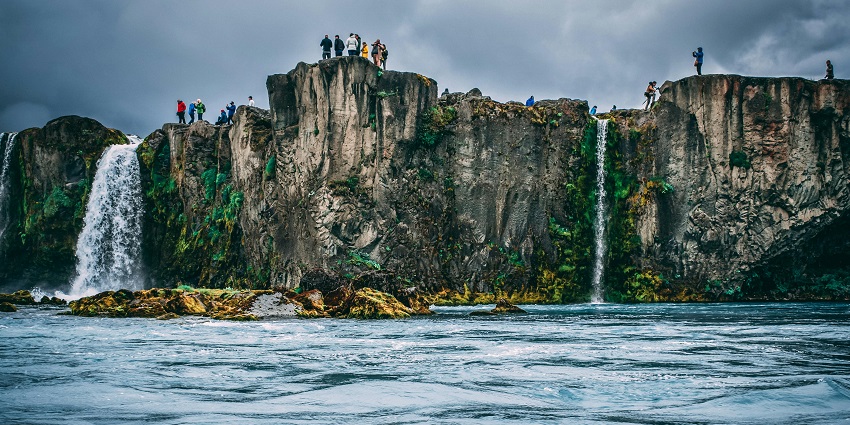A view of a sparkling water body with a lot of people standing on a cliff next to it.