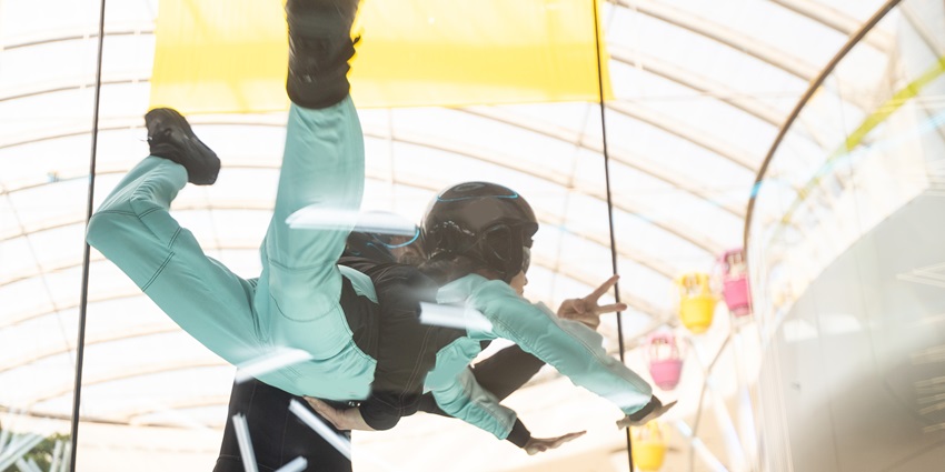 A mesmerising view of a girl doing indoor skydiving wearing a helmet and a blue suit.