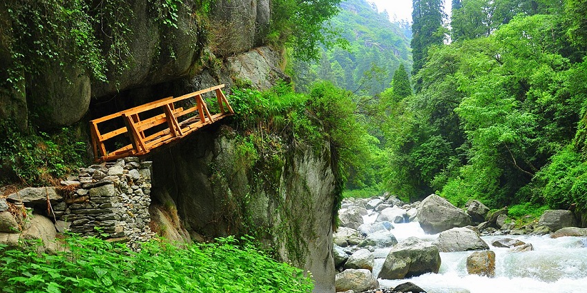 A bridge crossing over the sparkling stream beating through rocks amidst lush forests