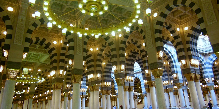 Interior view of Masjid-e-Nabawi showcasing ornate pillars, chandeliers, and Islamic art