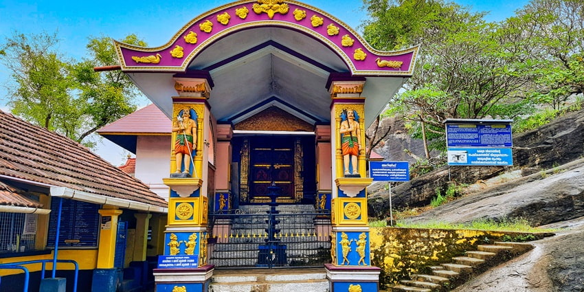 A frontal view of the entrance of a temple perched on top of a hill, with sculptures carved in pillars