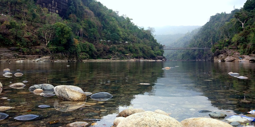 Scenic view of Jaflong with a clear river, lush green hills, and rocky shores - camping in Dawki.