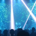 A fascinating view of a party in a club with blue lights and people performing in front.