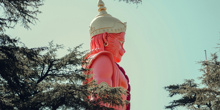 A breathtaking view of an idol of lord Hanuman surrounded by lush greenery during the day.