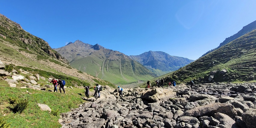 View of people climbing a lush green mountain with an alluring backdrop of clear skies.