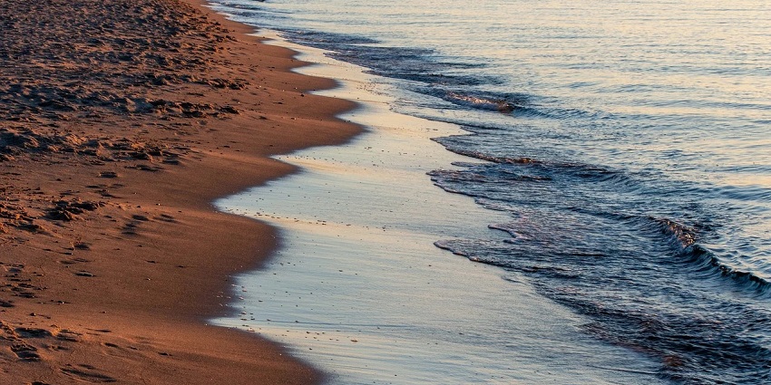 A scenic & captivating view of a beach with brown sand and gushing waves at the seashore.