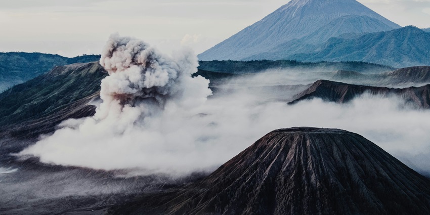 A breathtaking view of a volcano under dense fog with mountains in the background.