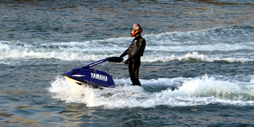 A person enjoying jet skiing in a water body nearby a beach on a s sunny day