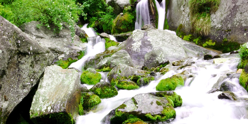 A picture of a stunning waterfall with water cascading down a rocky hill into a pond