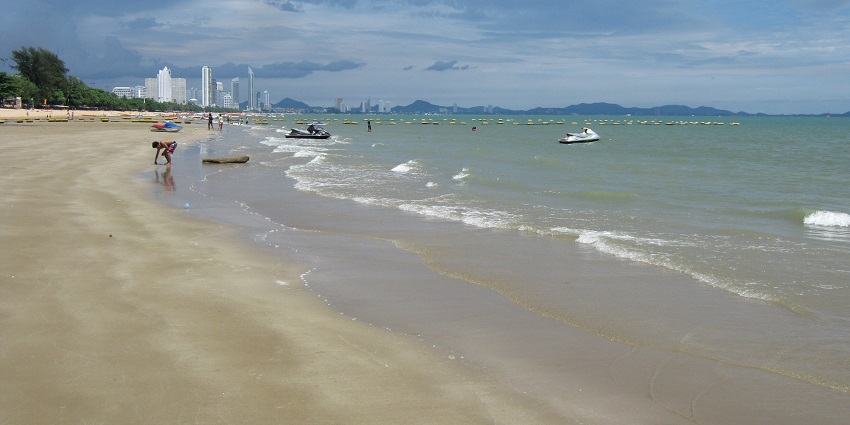 A picture of people enjoying a beach during day time with a view of skyscrapers in the background