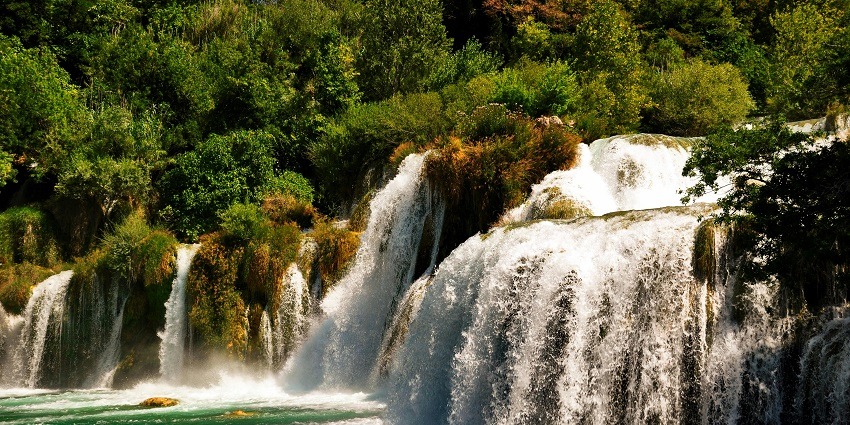 In frame, shimmering waters of Kaksen and Bhagsen Waterfalls surrounded by lush greenery.