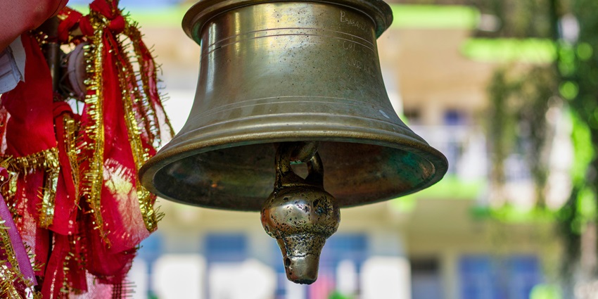 A stunning view of a golden bell in a temple with a red piece of cloth tied on the side.