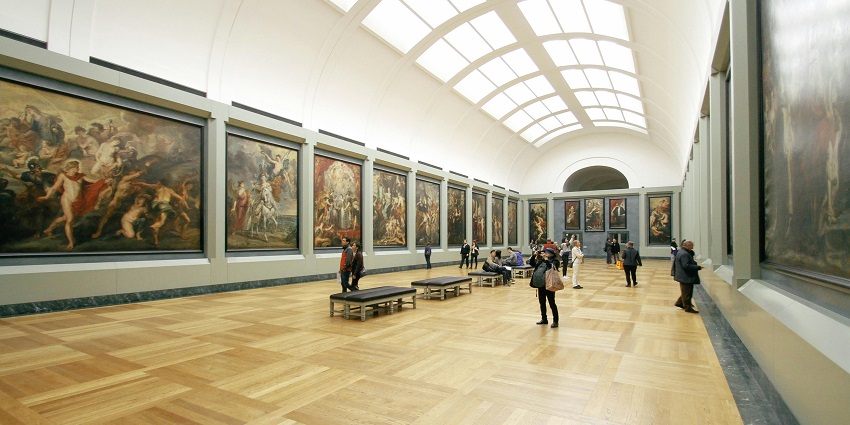 A picture of an art gallery with people admiring and exploring the various paintings and sculptures