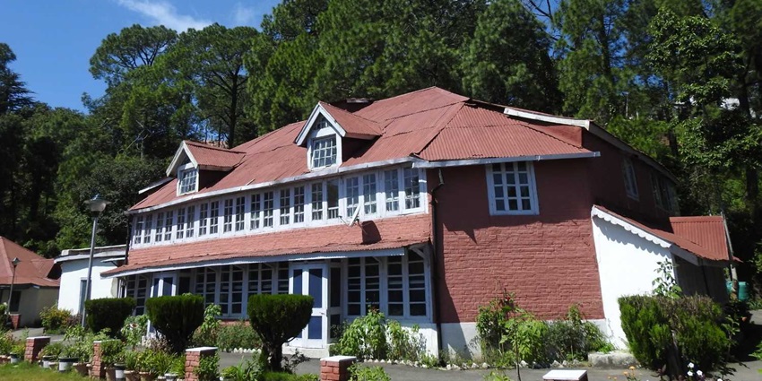 A beautiful British-style building in Kasauli with trees behind