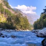 A picture of a river flowing through a village in Kasol with mountains on both sides